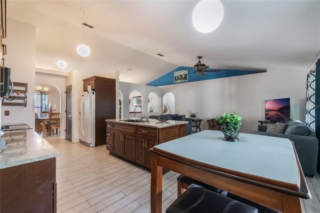 kitchen with pendant lighting, lofted ceiling, ceiling fan with notable chandelier, light stone countertops, and light hardwood / wood-style floors