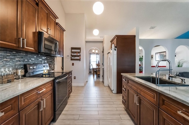 kitchen featuring light stone countertops, white refrigerator, black / electric stove, and sink