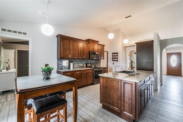 kitchen with sink, an island with sink, stainless steel appliances, and decorative light fixtures