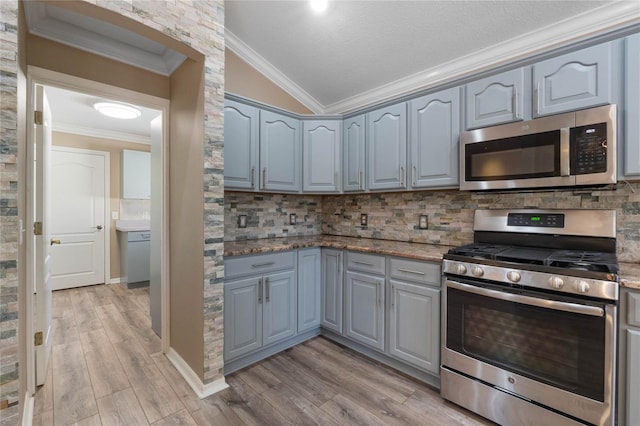 kitchen with tasteful backsplash, light wood-type flooring, stainless steel appliances, and vaulted ceiling