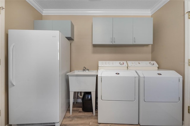 laundry room with cabinets, light hardwood / wood-style floors, crown molding, and washing machine and clothes dryer