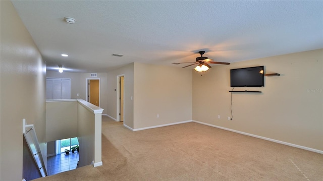 spare room featuring a textured ceiling, ceiling fan, and light carpet