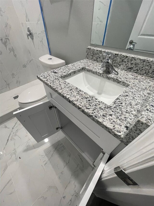 bathroom with a tile shower, vanity, and toilet