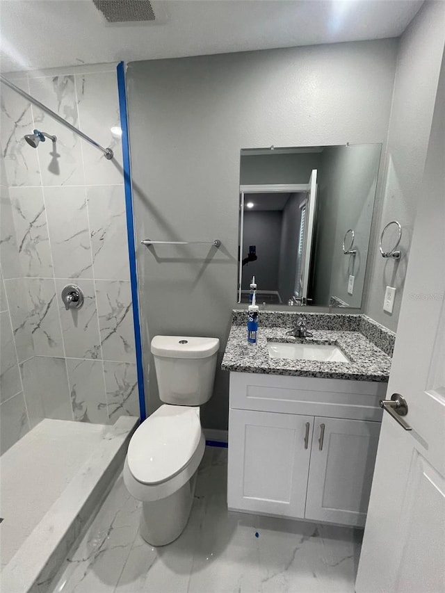 bathroom featuring a tile shower, vanity, and toilet