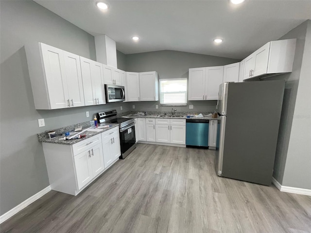 kitchen featuring stainless steel appliances, dark stone countertops, vaulted ceiling, white cabinets, and light wood-type flooring