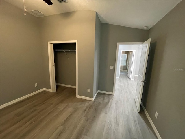 unfurnished bedroom featuring lofted ceiling, a walk in closet, ceiling fan, wood-type flooring, and a closet