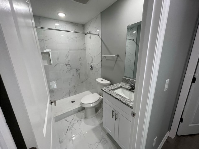 bathroom with a tile shower, vanity, and toilet