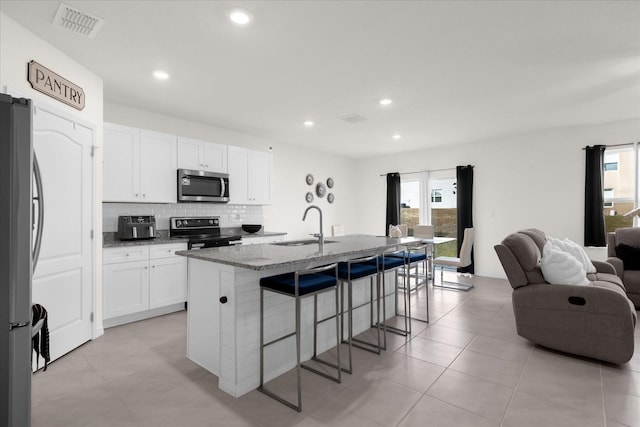 kitchen with a kitchen bar, light stone counters, stainless steel appliances, a center island with sink, and white cabinets