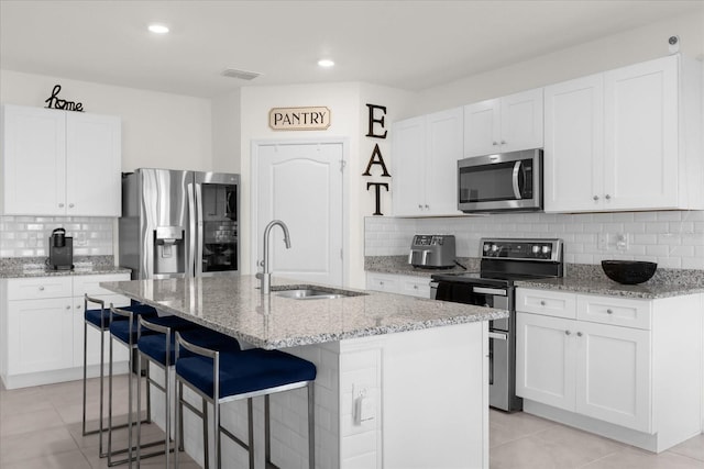 kitchen featuring light stone counters, stainless steel appliances, white cabinetry, a sink, and an island with sink