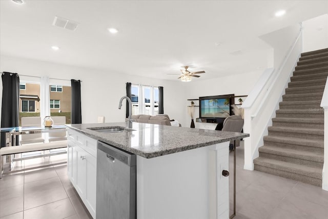 kitchen with light stone counters, a kitchen island with sink, a sink, white cabinets, and stainless steel dishwasher