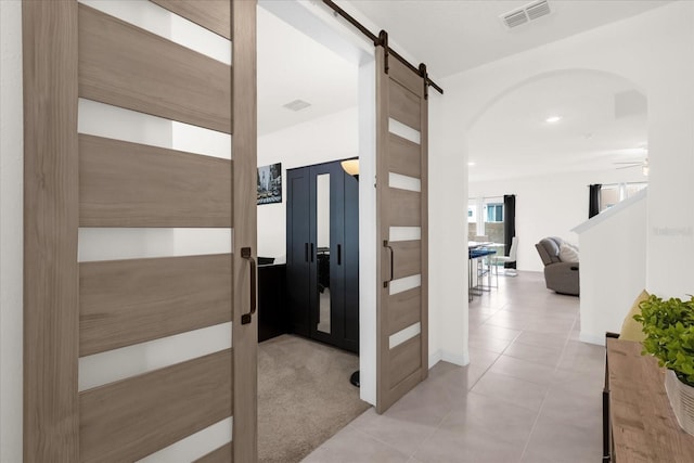 hallway with arched walkways, a barn door, light tile patterned floors, and visible vents