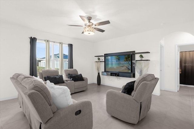 living area with arched walkways, light tile patterned flooring, ceiling fan, and baseboards