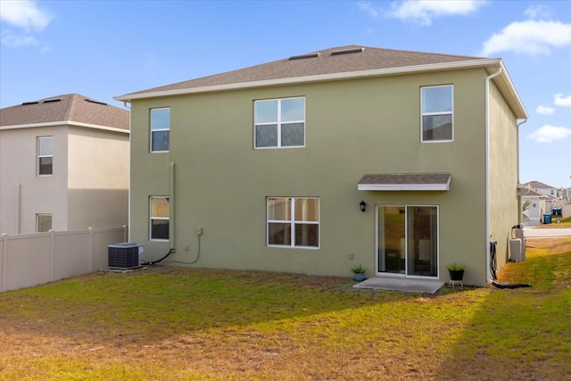 rear view of property featuring central AC, a lawn, fence, and stucco siding