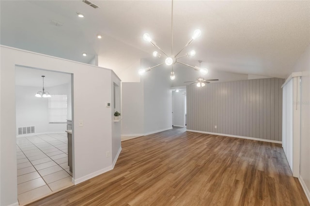 unfurnished living room with lofted ceiling, ceiling fan with notable chandelier, wooden walls, a textured ceiling, and wood-type flooring