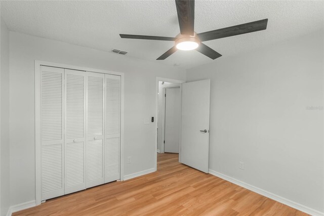 unfurnished bedroom with ceiling fan, light wood-type flooring, a textured ceiling, and a closet