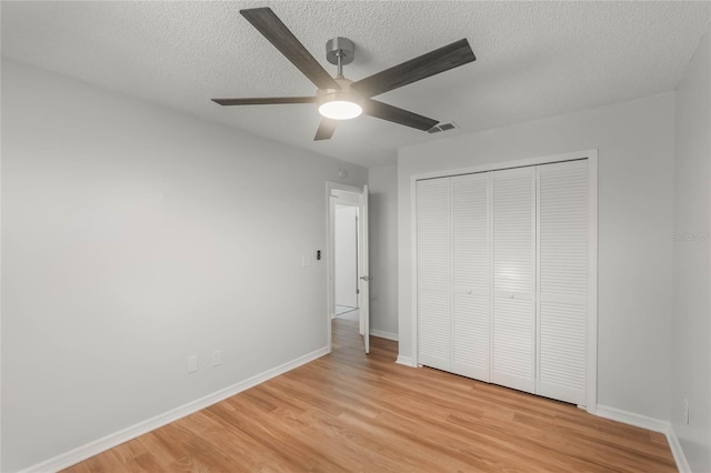 unfurnished bedroom with ceiling fan, a closet, a textured ceiling, and light hardwood / wood-style flooring