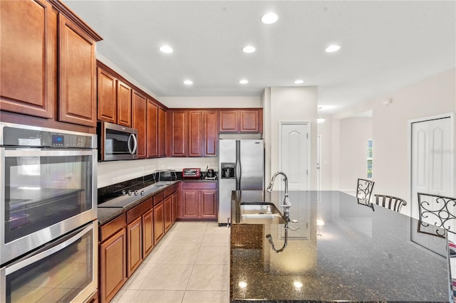 kitchen with sink, a breakfast bar area, dark stone countertops, light tile patterned floors, and stainless steel appliances