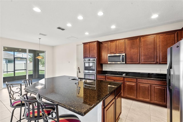 kitchen featuring a kitchen island with sink, light tile patterned floors, pendant lighting, and appliances with stainless steel finishes