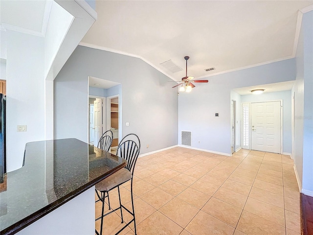 kitchen featuring ceiling fan, dark stone countertops, crown molding, a kitchen bar, and light tile patterned floors