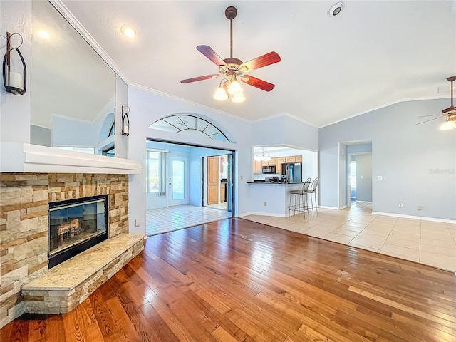 unfurnished living room featuring ceiling fan, a stone fireplace, ornamental molding, and light hardwood / wood-style flooring