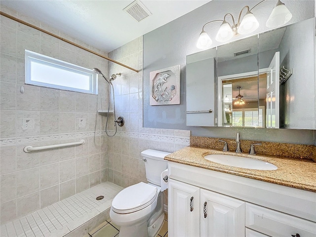 bathroom featuring a tile shower, vanity, toilet, and tile walls