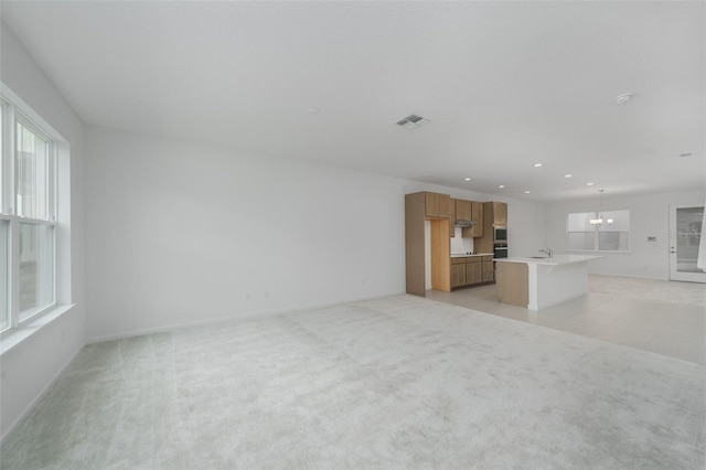 unfurnished living room with light carpet, sink, and a notable chandelier