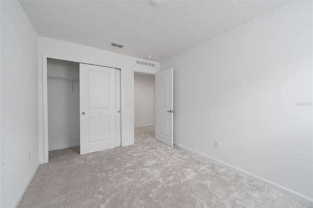 unfurnished bedroom featuring light colored carpet, a textured ceiling, and a closet