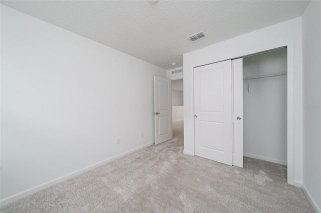 unfurnished bedroom featuring light colored carpet, a textured ceiling, and a closet