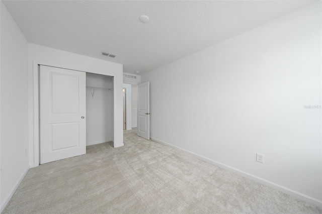 unfurnished bedroom with a closet, light colored carpet, and a textured ceiling