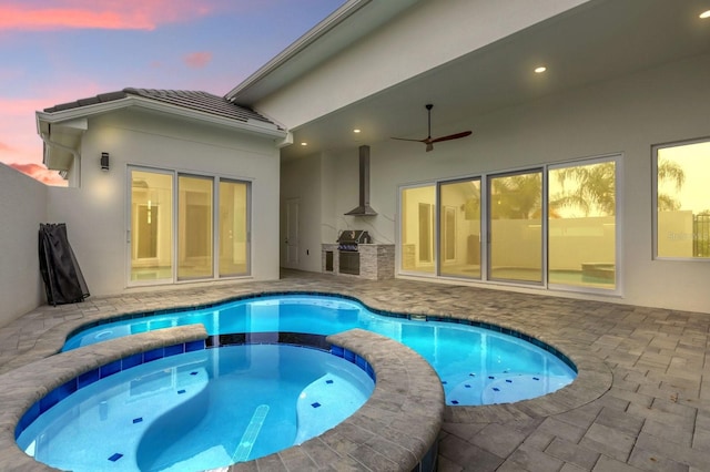 pool at dusk with a patio area, an in ground hot tub, area for grilling, and exterior kitchen