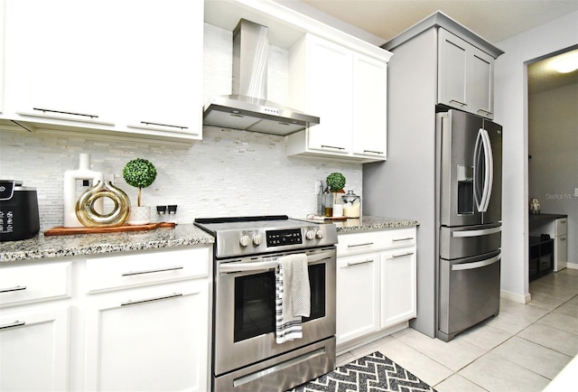 kitchen featuring light stone countertops, tasteful backsplash, stainless steel appliances, wall chimney range hood, and light tile patterned floors