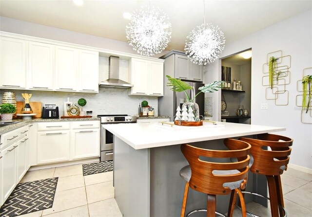 kitchen with a center island, wall chimney range hood, a kitchen breakfast bar, a notable chandelier, and appliances with stainless steel finishes