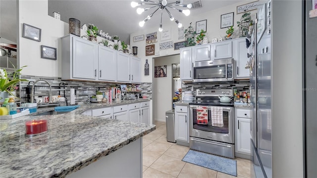 kitchen with white cabinetry, stainless steel appliances, light tile patterned floors, light stone countertops, and a chandelier