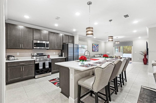 kitchen featuring hanging light fixtures, stainless steel appliances, plenty of natural light, and a center island with sink