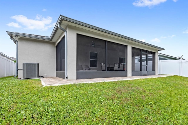 rear view of property with a yard, stucco siding, central air condition unit, a sunroom, and fence