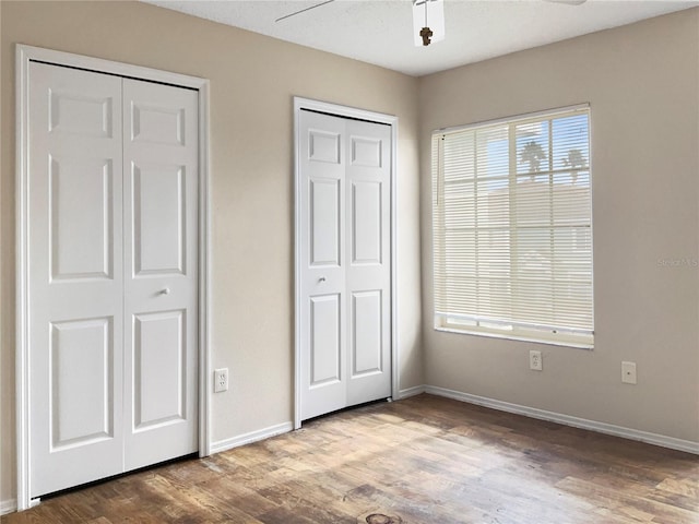 unfurnished bedroom with ceiling fan, hardwood / wood-style floors, and two closets