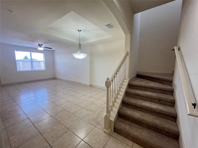 stairs featuring a tray ceiling, tile patterned floors, and ceiling fan