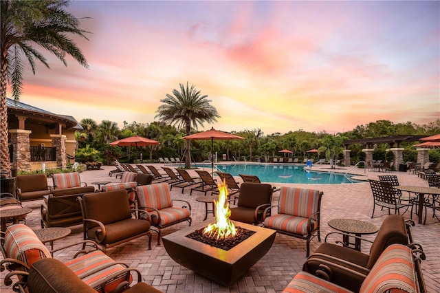 pool at dusk featuring an outdoor living space with a fire pit and a patio