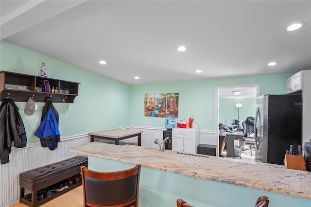 kitchen with light stone countertops, white cabinetry, stainless steel refrigerator, and light hardwood / wood-style floors