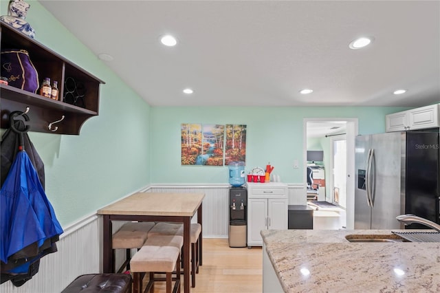 kitchen featuring light stone countertops, sink, stainless steel refrigerator with ice dispenser, light hardwood / wood-style floors, and white cabinets