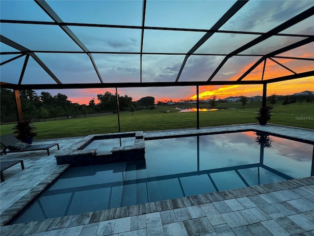 pool at dusk featuring an in ground hot tub, a lanai, a patio area, and a lawn