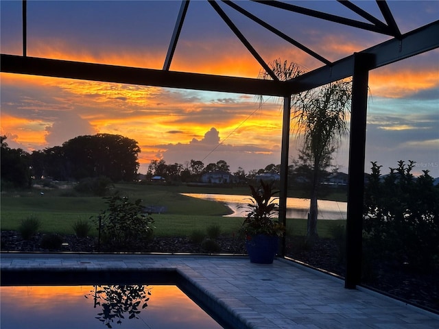 pool at dusk featuring a yard, a patio area, and a water view