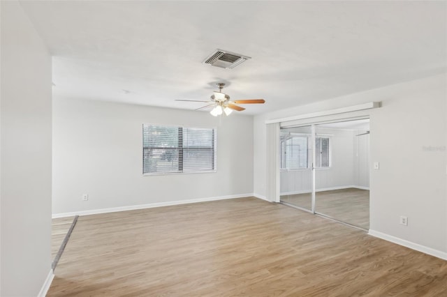 unfurnished bedroom with ceiling fan, light hardwood / wood-style flooring, a closet, and multiple windows