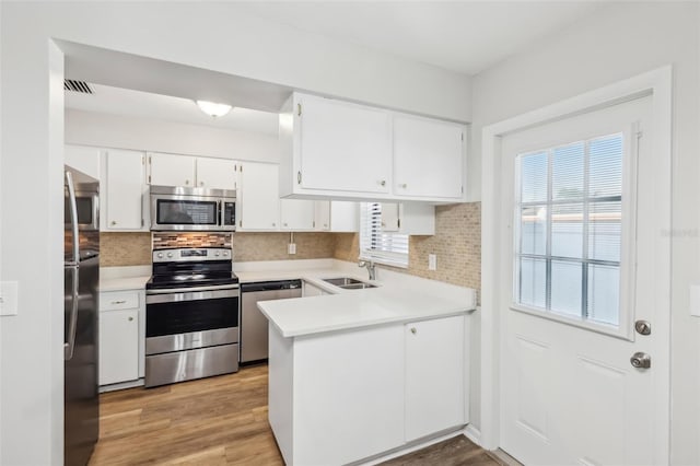 kitchen with light hardwood / wood-style floors, decorative backsplash, white cabinets, appliances with stainless steel finishes, and sink