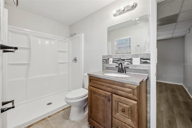 bathroom with toilet, a paneled ceiling, backsplash, a shower, and vanity