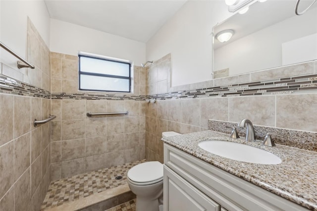 bathroom with toilet, a tile shower, and vanity