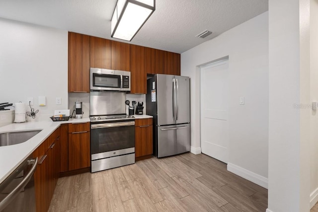 kitchen featuring a textured ceiling, light wood-type flooring, stainless steel appliances, and sink