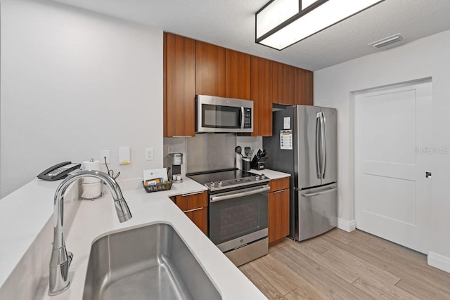 kitchen featuring a textured ceiling, light wood-type flooring, sink, and appliances with stainless steel finishes