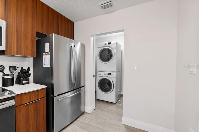 kitchen featuring stainless steel appliances, light hardwood / wood-style flooring, stacked washing maching and dryer, and a textured ceiling