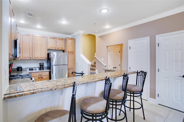 kitchen with light brown cabinets, light stone counters, kitchen peninsula, and appliances with stainless steel finishes